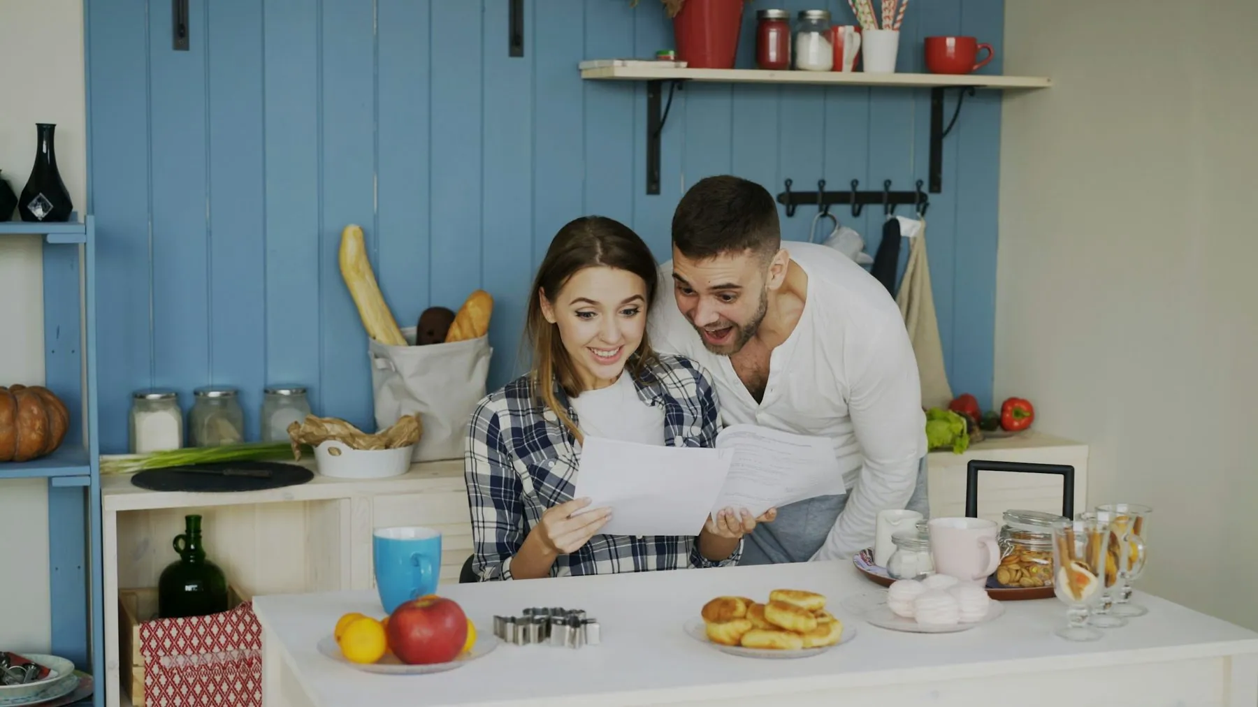 Attractive happy couple recieve good news unfolding letter in the kitchen while have breakfast at home early morning