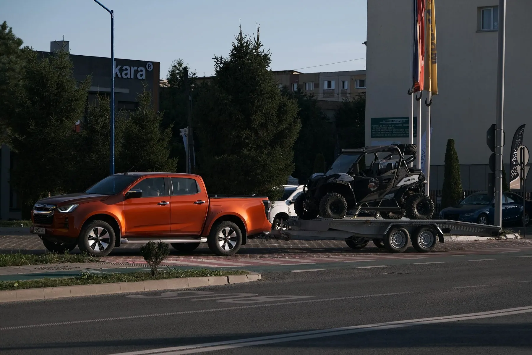 Description: An orange pickup truck parked on a street, towing an off-road vehicle on a trailer in a suburban area.