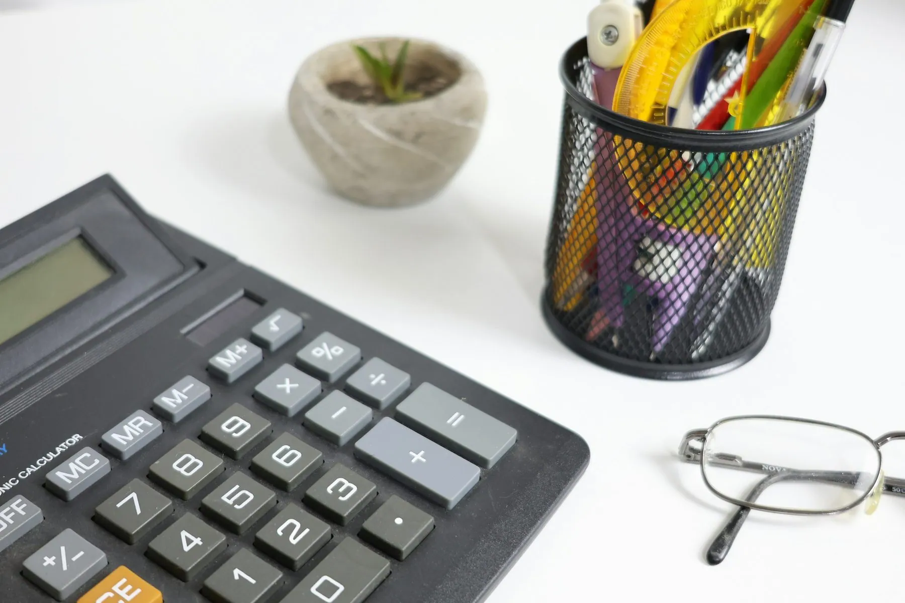 Calculator, glasses, and pens on a white desk